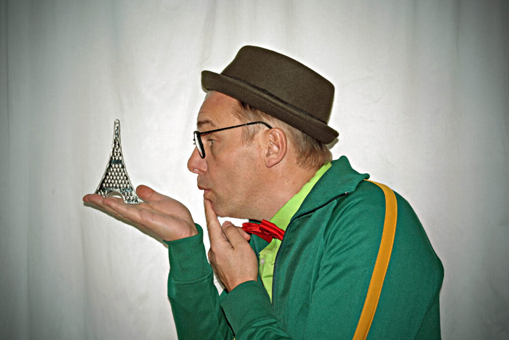 Jens Heuwinkel in seiner Rolle aus "Sauresani" schaut auf eine Miniaturausgabe des Pariser Eiffelturms.